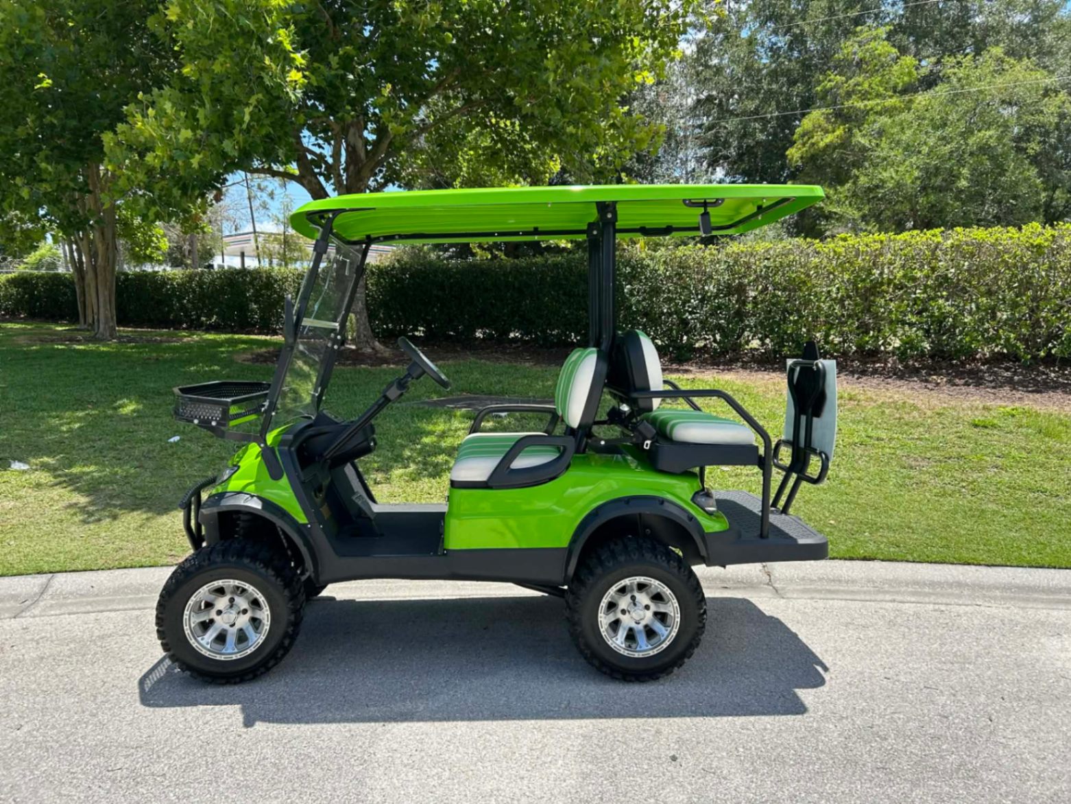 Side view of bright green luxury golf cart with striped seats parked by a resort lawn